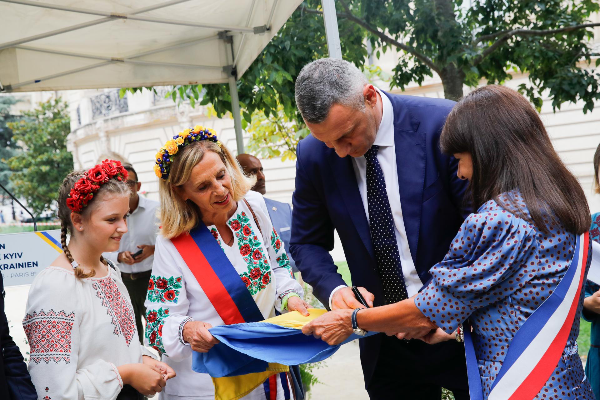 El alcalde de Kiev, Vitali Klitschko (2d) junto a la alcaldesa de París, Anne Hidalgo, (d) firma una bandera ucraniana durante la inauguracióndel 2Jardín de Kiev al pueblo ucraniano"./ EFE