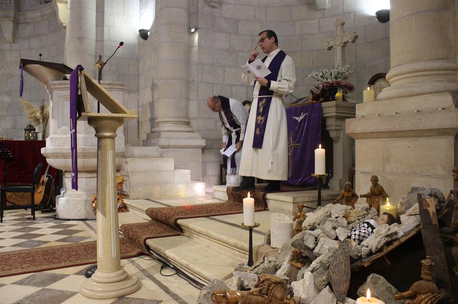 El reverendo Munther Isaac durante una misa junto al nacimiento con un Niño Jesús entre ruinas en Belén (Cisjordania). / EFE